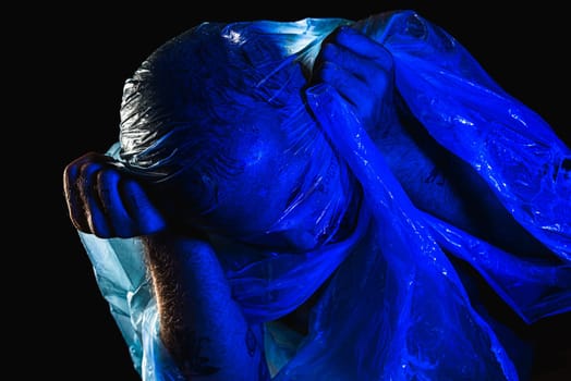 Man with plastic bag over his head, suffocated. Studio shot with blue filter. Isolated on black background.