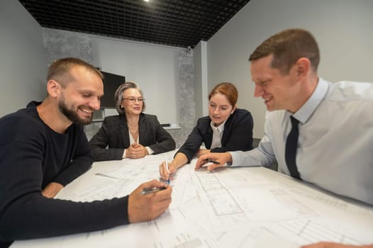 Four business people sitting around a table discussing blueprints. Designers engineers at a meeting