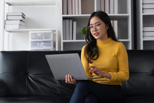 Image of smiling happy beautiful asian woman relaxing using of laptop computer while sitting on desk woman creative girl working at home concept.