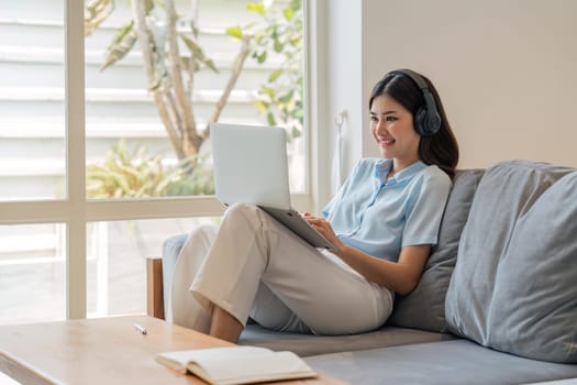 Image of smiling happy beautiful asian woman relaxing using of laptop computer while sitting on desk woman creative girl working at home concept.