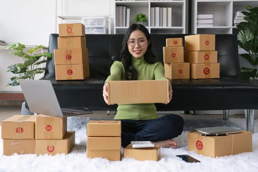 Young business woman working online e-commerce shopping at home. Young woman seller prepare parcel box of product for deliver to customer. Online selling.