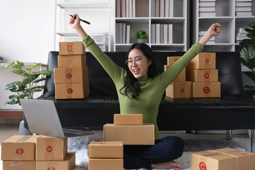 Happy young Asian woman entrepreneur, Smile for sales success after checking order from online shopping store in a laptop at home office, Concept of merchant business online.