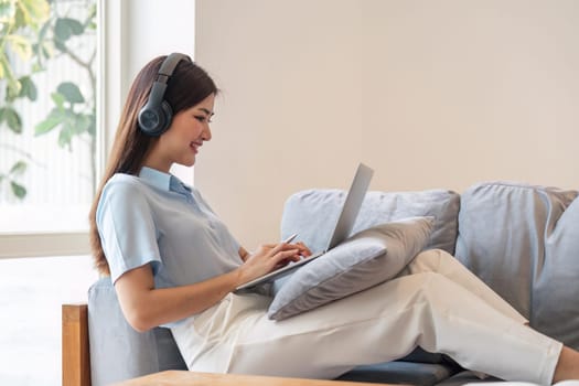 Image of smiling happy beautiful asian woman relaxing using of laptop computer while sitting on desk woman creative girl working at home concept.