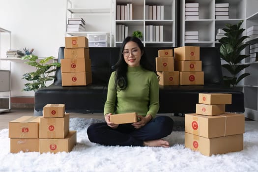 Young business woman working online e-commerce shopping at home. Young woman seller prepare parcel box of product for deliver to customer. Online selling.
