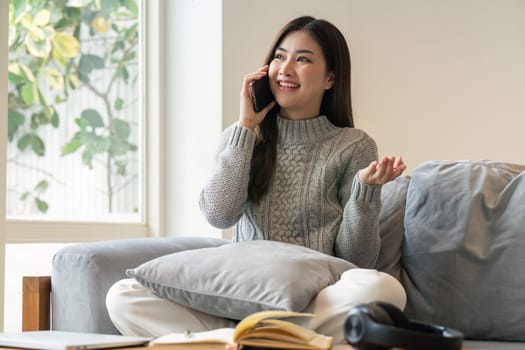 young woman talking on phone in her cosy house. Businesswoman working from home office and using cell phone. Beautiful woman sitting at the sofa in a home.