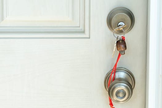 A key with a keychain on a red rope is inserted into the door lock.