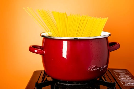 spaghetti in a saucepan. a beautiful red saucepan with spaghetti. cooking spaghetti in a saucepan on a gas stove. homemade Italian-style dinner. kitchen saucepan on a orange background
