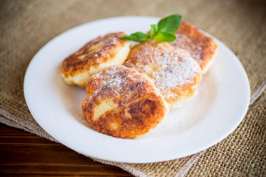 Sweet cooked cheesecakes in powdered sugar in a plate on the table.