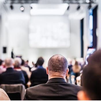 Speaker giving a talk in conference hall at business event. Rear view of unrecognizable people in audience at the conference hall. Business and entrepreneurship concept