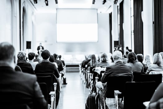 Speaker giving a talk in conference hall at business event. Rear view of unrecognizable people in audience at conference hall. Business and entrepreneurship concept. Black and white selenium image.