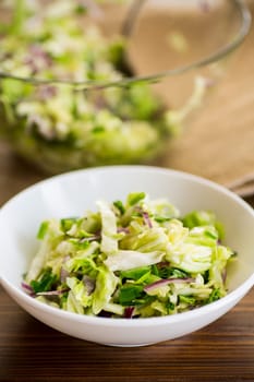 Young cabbage salad with purple onions in a bowl on a wooden table.