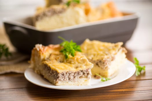 Cooked meat pie, pieces in a plate on a wooden table.