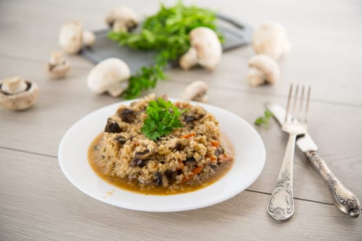 cooked bulgur with mushrooms, carrots and vegetables in a plate, on a wooden table.
