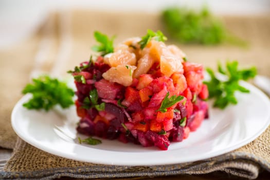 vinaigrette salad of boiled vegetables with salted fish in a plate, on a wooden table.