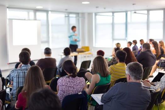 Business and entrepreneurship symposium. Speaker giving a talk at business meeting. Audience in conference hall. Rear view of unrecognized participant in audience.