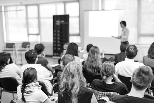 Business and entrepreneurship symposium. Speaker giving a talk at business meeting. Audience in conference hall. Rear view of unrecognized participant in audience.