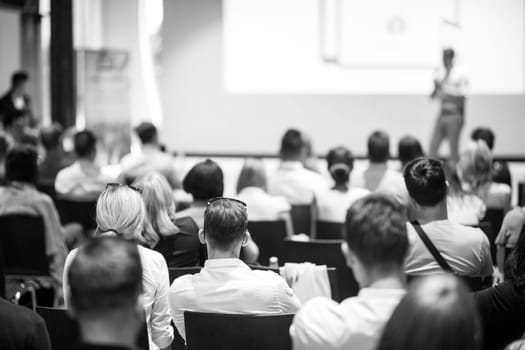 Speaker giving a talk in conference hall at business event. Focus on unrecognizable people in audience. Business and Entrepreneurship concept. Black and white image.