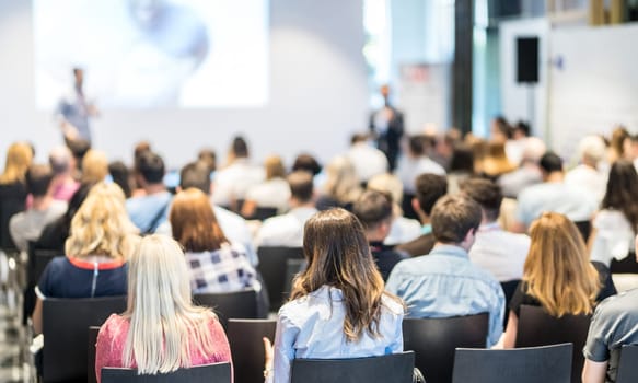 Speaker giving a talk in conference hall at business event. Audience at the conference hall. Business and Entrepreneurship concept. Focus on unrecognizable people in audience.