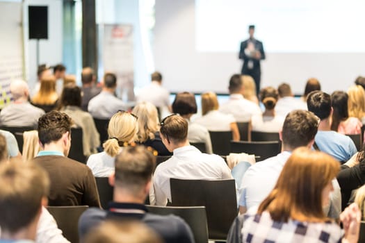 Speaker giving a talk in conference hall at business event. Audience at the conference hall. Business and Entrepreneurship concept. Focus on unrecognizable people in audience.