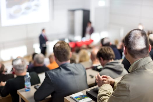 Speaker giving a talk in conference hall at business event. Audience at the conference hall. Business and Entrepreneurship concept. Focus on unrecognizable people in audience.