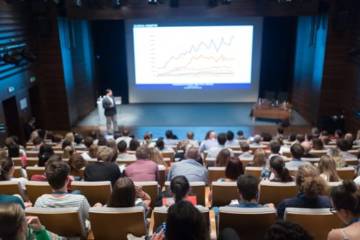 Business and entrepreneurship symposium. Speaker giving a talk at health care workshop meeting. Audience in conference hall. Rear view of unrecognized participant in audience.