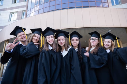 Happy students in graduate gown stand in a row against the backdrop of the university