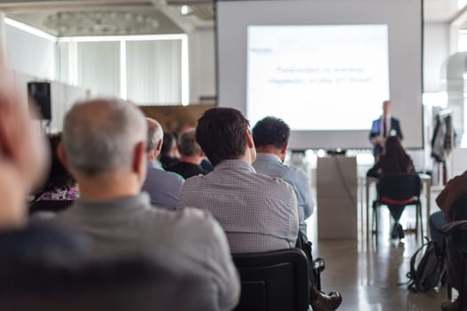 Speaker giving a talk in conference hall at business event. Audience at the conference hall. Business and Entrepreneurship concept. Focus on unrecognizable man in the audience.