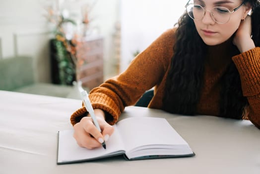 Woman writing in copybook. Business woman or young female student holding pen in hand writing in paper notebook journal, taking notes studying, doing homework, making checklist. Close up view.