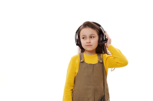 Adorable primary school student, Caucasian 5-6 years lovely little child girl in casual clothes, wearing audio headset, isolated white background. Online communication. Distance education. E-learning