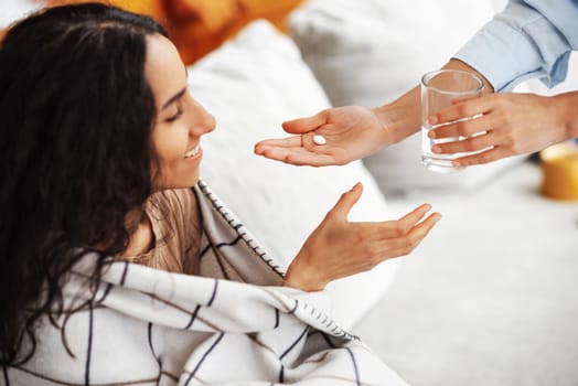 Arab young woman is happy to receive care and treatment. Gets a pill from a specialist. Woman smiling and looking at a pill. She stretches her hand to a glass of water, ready to take the treatment.