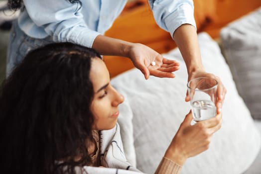 Specialist gives a pill and a glass of water so that a young woman of Arab appearance can take the treatment. Care and home comfort. On the palm of a pill, transferring a glass from hand to hand.
