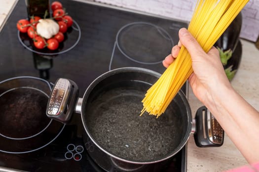 Closeup of spaghetti in pot on stove. the cook's hand drops the spaghetti into a saucepan of boiling water. Pasta cooking