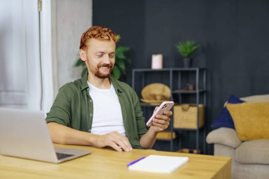 Programmer man with red foxy hair, sitting at desk in a cozy home interior. He working on laptop, emphasizing the concept of freelance work and the ability to work from home. . High quality photo