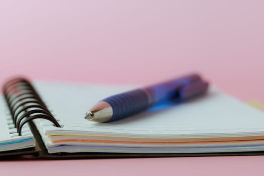 Selective focus of a pen on a notebook against pink background for the concept of work and study.