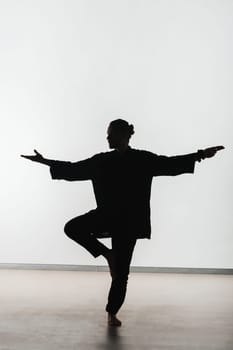 Silhouette of a person practicing qigong energy exercises on a light background.