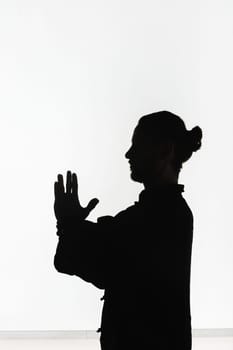 Silhouette of a person practicing qigong energy exercises on a light background.