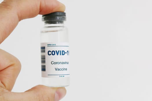 A sealed glass vial of covid-19 vaccine in the hand of a scientist or physician to observe and prepare for injection into the population.