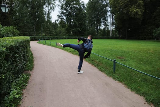 A young man dressed in blue with a backpack and white shoes put his foot up in the road. The boy is doing physical exercise while hiking.