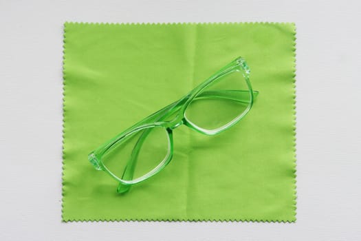 Folded glasses with a green transparent frame lie on a green cleaning cloth.