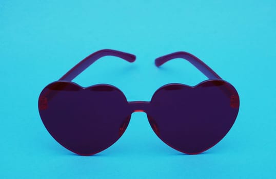 Heart-shaped glamor glasses in dark red color in the shape of a heart on a blue paper background.