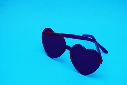 Heart-shaped glamor glasses in dark red color in the shape of a heart on a blue paper background.