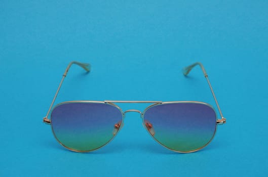 Sunglasses in a yellow thin metal frame with a blue and yellow gradient on a blue background.