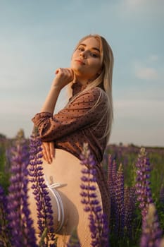 A beautiful woman in a straw hat walks in a field with purple flowers. A walk in nature in the lupin field.