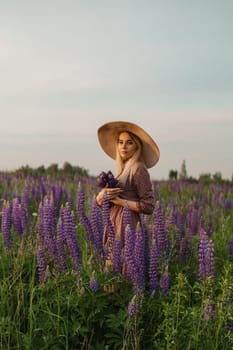 A beautiful woman in a straw hat walks in a field with purple flowers. A walk in nature in the lupin field.