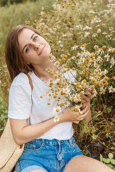 Beautiful young woman in nature with a bouquet of daisies. Field daisies, field of flowers. Summer tender photo.