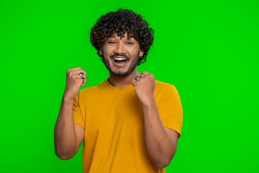 Happy joyful indian man shouting, raising fists in gesture I did it, celebrating success, winning, birthday, lottery jackpot goal achievemen, good news. Young hindu guy on green chroma key background