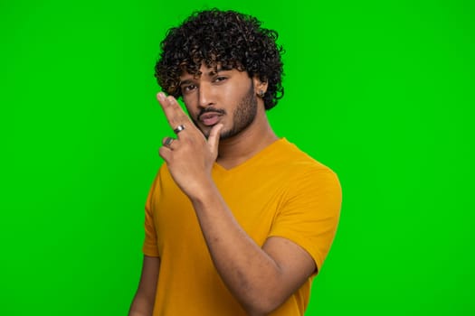 Happy young indian man pointing around with finger gun gesture, looking confident, making choice, shooting killing with hand pistol right on target. Hindu guy isolated on green chroma key background