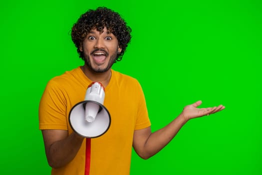 Indian man talking with megaphone, proclaiming news, loudly announcing advertisement, warning using loudspeaker to shout speech, pointing empty place. Copy-space. Handsome guy on chroma key background