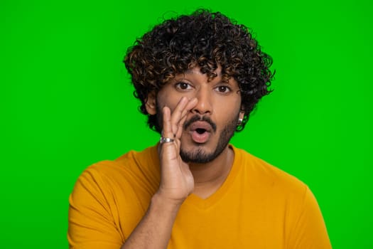 Keep my secrets, silence. Indian man whisper news rumors holding hands near mouth, share gossip, quiet. Hindu guy telling interesting confidential story isolated on green chroma key background indoors
