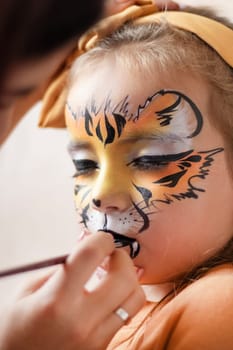 Cute makeup little tiger. face painting outdoors, having fun, copy space. girl with aqua makeup of tiger muzzle. Master making aqua makeup on girl face. aqua grimm on birthday or halloween party